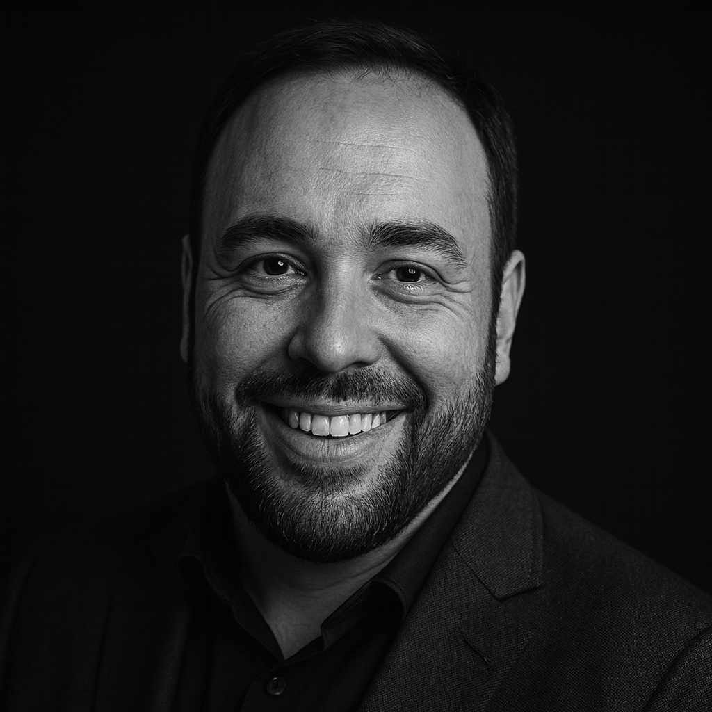 Matt Howard, smiling, in a dark jacket against a black background